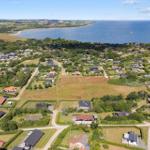 Aerial view of coastal village with houses, greenery, and sea in background.