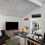 Wohnzimmer mit Sofa, Fernseher und Tisch. Durchgehende Fenster zur Terrasse.