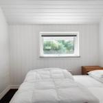Ein Schlafzimmer mit weißer Wandverkleidung, einem Bett und einem Fenster mit Blick auf Grün.
