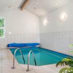 Innere Schwimmhalle mit Pool, Holzbank, Fenster und Pflanze.