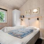 Schlafzimmer mit Bett, Fenster und Holzwandverkleidung.