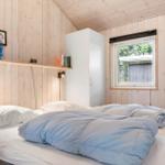 Schlafzimmer mit Bett, Fenster und weißen Schränken an Holzwänden.