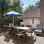 Terrasse mit Tisch, Stühlen und blauem Sonnenschirm. Hintergrund: Haus mit Ziegeldach und Holzgeländer.