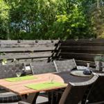 Holztisch mit Stühlen und Pflanzen auf einer Terrasse mit Holzgeländer.