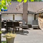Terrasse mit Holzdielen, Gartenmöbeln und Holzstapel an der Wand.