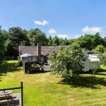 Haus mit Garten, Terrasse und Grillplatz unter blauem Himmel.
