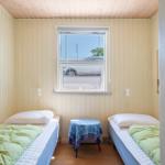 Zwei Einzelbetten mit grünen Decken, ein Tisch mit Tischdecke und ein Fenster.