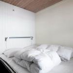 Ein Bett mit weißen Kissen und Decke, Wand mit vertikalen weißen Paneelen und Holzdecke.