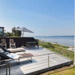 Terrasse mit Liegestühlen, Tisch und Sonnenschirm am Wasser.