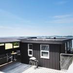 Schwarzes Haus mit Terrasse, Grill und Blick auf Wasser.