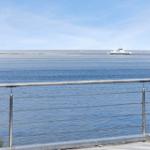 Blick auf das Meer mit einem Schiff in der Ferne und einer Metallbrüstung im Vordergrund.
