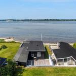 Haus mit Terrasse am Wasser, umgeben von Grünfläche und Blick auf die Bucht.