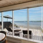 Große Glasfront mit Blick auf den See und Terrasse mit Liegestühlen und Sonnenschirm.