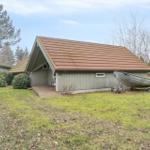 Ein kleines Haus mit braunem Dach und Holzveranda. Ein Boot steht auf einem Anhänger im Gras.
