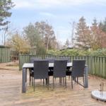 Terrasse mit Esstisch und Stühlen, umgeben von Grünfläche und Zaun.