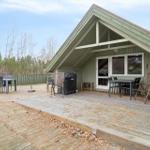 Holzterrasse mit Grill, Tischen und Stühlen vor einem Haus mit Dachüberstand.