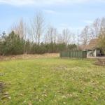 Grüner Garten mit Holzgeländer und Terrasse. Im Hintergrund Bäume und ein Haus.