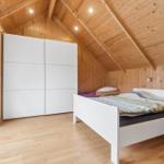 Schlafzimmer mit weißem Bett, Schwebetüren und Holzwandverkleidung unter schrägem Dach