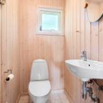 Badezimmer mit Toilette, Waschbecken und kleinem Fenster. Holzwandverkleidung und Fliesenboden.