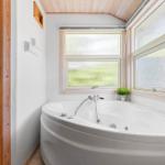 Eckbadewanne mit Duschbrause, zwei Fenstern und Holzverkleidung an der Wand.