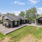 Moderne schwarze Holzhütte mit großem Balkon und Grillplatz im Garten.