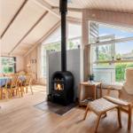 Wohnbereich mit Kamin, Sitzgelegenheit und Blick auf Garten. Küche und Essbereich sind sichtbar.