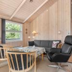 Wohnzimmer mit Sofa, Sessel und Tisch. Holzwände und -decke. Fenster mit Blick auf Grün.