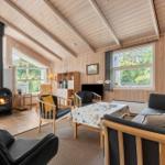 Wohnzimmer mit Holzdecke, Kamin, Sofa und Sitzgelegenheiten. Große Fenster mit Blick auf Garten.