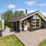 Schwarzes Holzhaus mit Terrasse und Garten. Große Fenster, Außentisch und Schaukel.