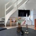 Runde Tisch mit Blumen, Kerze und Glas. Im Hintergrund Stuhl, Fernseher und Kühlschrank.
