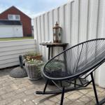 Schwarze Schaukelstuhl auf Terrasse mit Pflanzen und Laterne an weißer Wand.