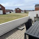 Terrasse mit Tisch und Stühlen, weißer Zaun, Blick auf Gras und Häuser