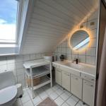 Badezimmer mit Dachfenster, Waschbecken, Spiegel und Toilette.