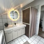 Badezimmer mit Waschtisch, Spiegel und Dusche mit Vorhang.