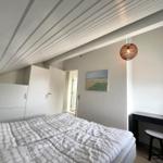 Schlafzimmer mit Bett, Kleiderschrank, Schreibtisch und Pendelleuchte unter schrägem Dach.