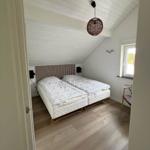 Schlafzimmer mit Doppelbett, Holzboden und schrägem Dach. Fenster und Hängelampe sichtbar.