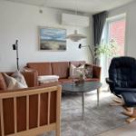 Wohnzimmer mit braunem Sofa, schwarzer Sessel und Tisch. Wandbild und Fenster sichtbar.