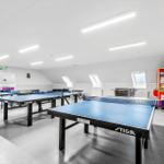 Raum mit mehreren Tischtennisplatten und einer Spielzeugmaschine.