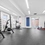 Fitnessraum mit Klimaanlage, Gewichten, Fahrradtrainer und Kettlebells.