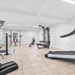 Fitnessraum mit Laufband, Kraftstation und Trainingsgeräten auf gefliestem Boden.