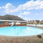 Runder Pool mit Rutsche vor einem Backsteinhaus unter blauem Himmel.