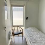Schlafzimmer mit Bett, Stuhl und Fenster. Holzfußboden und Deckenleuchte.