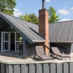 Haus mit Terrasse, Liegestühlen und Schornstein. Holzverkleidung und graue Dächer.