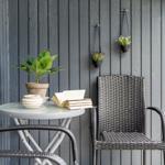 Terrasse mit Tisch, Stühlen und Pflanzen an grauer Holzwand.