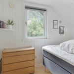 Schlafzimmer mit Dachbodenfenster, Bett und Holzschrank. Wand mit Bildern und Pflanze.