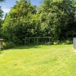 Grüner Garten mit Schaukel und Zaun. Hintergrund: dichter Wald.