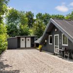 Holzhaus mit Terrasse, Grill und Grillplatz. Umgeben von Bäumen und Gras.