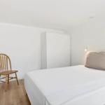 Ein Schlafzimmer mit Bett, Kleiderschrank und Stuhl. Wandlampe und Korb an der Wand.