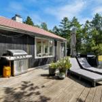 Terrasse mit Grill, Liegen und Pflanzen vor einem Haus mit Holzfassade.