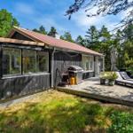 Ein Haus mit Holzveranda, Grill und Liegen im Grünen.